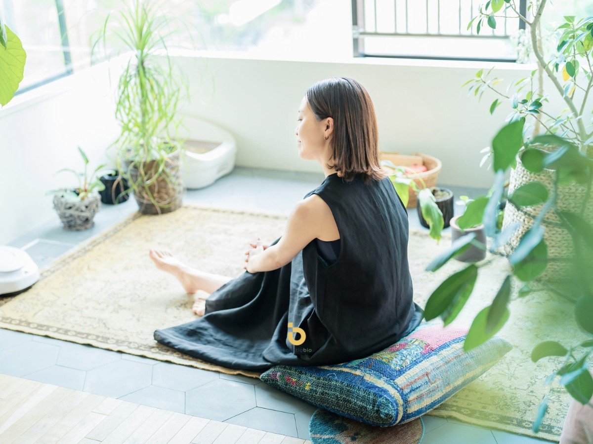 Woman meditating at home surrounded by indoor plants and natural light